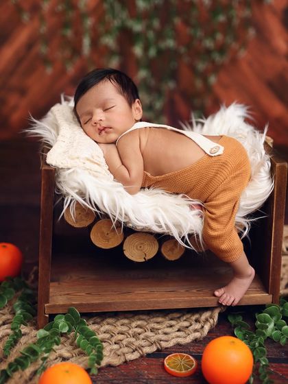 A rustic, nature-inspired setup with a baby boy in overalls sleeping on a log-style hammock, surrounded by oranges for a pop of color.