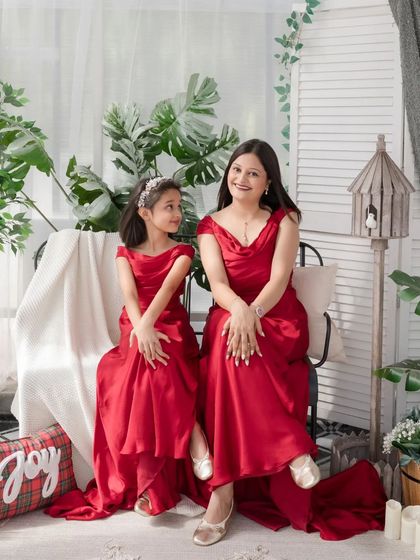 A lovely seated portrait of a mother and daughter in matching red dresses.