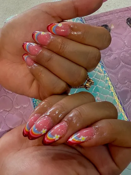 Let your nails show your playful side. This custom design features a modern rainbow French tip on a sheer pink base, accented with tiny, hand-painted daisies for a cheerful and unique look.