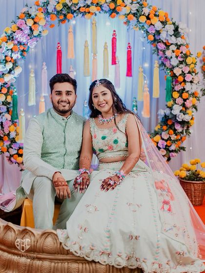 A lovely formal portrait of the couple at their Haldi ceremony, seated in front of the beautiful floral decor.