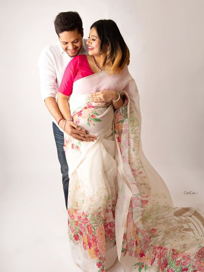 A bright and happy couple's portrait. The mom-to-be wears a beautiful floral saree, and her partner's joy is unmistakable.