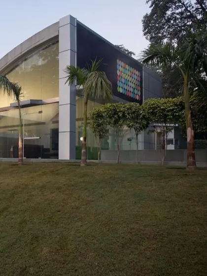 The exterior view of the completed adaptive reuse project shows how modern cladding and a large digital art installation were integrated with the original structure. The surrounding green mounds and palm trees soften the building's form, grounding it in its environment.