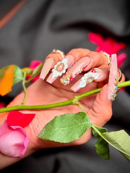 Elegant and romantic nail art, featuring nude tones, 3D white flowers, and sparkling rhinestones.