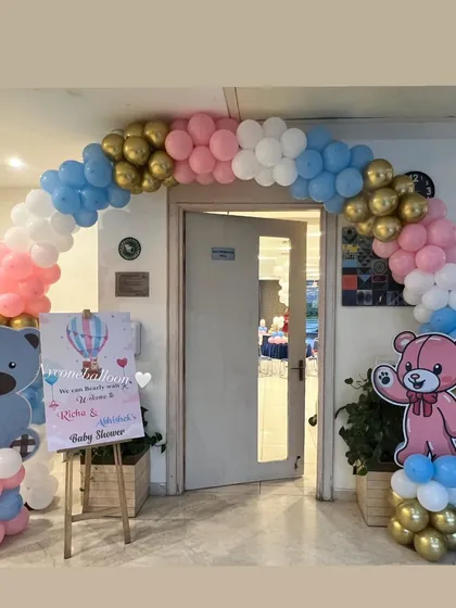 Welcome your guests in style with a themed entrance arch. This balloon arch for a teddy bear baby shower uses pink, blue, and gold balloons and includes a personalized welcome sign for the parents-to-be.