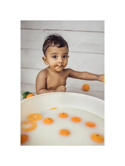 A playful baby reaches for an orange from his milk bath, making a cute face. This candid moment captures the fun and spontaneity of our fruit bath sessions.