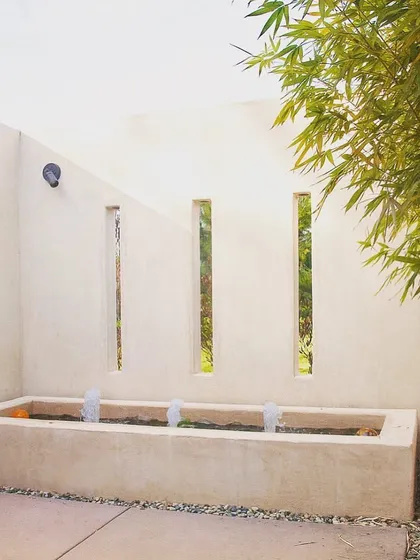 This is a contemporary fountain I designed and installed. The minimalist concrete basin, bamboo accent, and vertical slat cutouts in the wall create a modern and tranquil water feature.