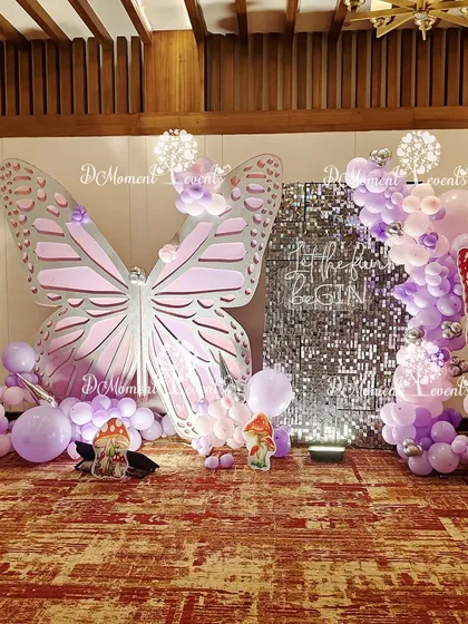 A glamorous photo booth combining a giant butterfly prop with a shimmering silver sequin wall. The purple and pink balloon garland adds a pop of color, making it a perfect spot for photos.