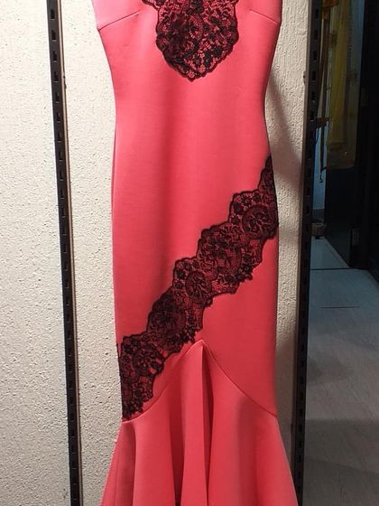 A striking coral mermaid-style gown with black lace appliqué. This body-hugging silhouette is designed to make a bold fashion statement at any formal occasion.