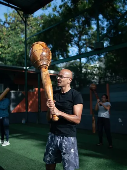 A member holds a large Gada, a look of accomplishment on his face. The sunny, outdoor setting highlights the enjoyable and rewarding nature of our training sessions.