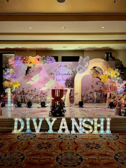Here is a full stage setup for an enchanted butterfly themed first birthday. The design includes a custom backdrop with fairy silhouettes, large marquee letters for the child's name, and elegant balloon garlands to create a magical atmosphere.