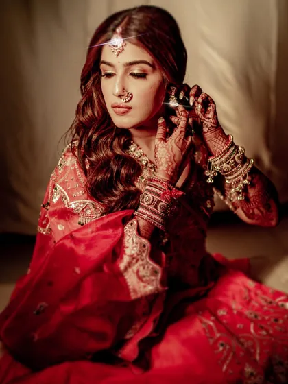 The bride adjusts her earring in a quiet, reflective moment. The soft lighting enhances the romantic feel of this look, with her wavy hair and glowing makeup.
