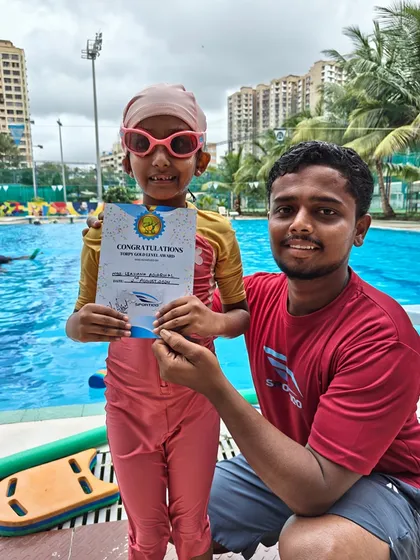 A smiling young girl in a pink swim cap receives her certificate from her coach, a proud moment for both student and instructor.