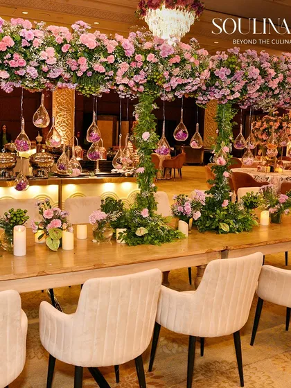 A stunning wedding dining setup featuring tables laden with lush pink floral arrangements and hanging glass ornaments. We craft immersive environments that blend romance and opulence.