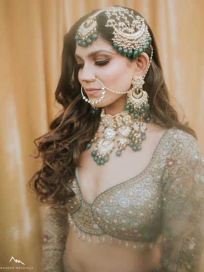 A detailed shot of the bride's profile, focusing on her intricate jewelry and the soft, smokey eye makeup that complements the green stones.
