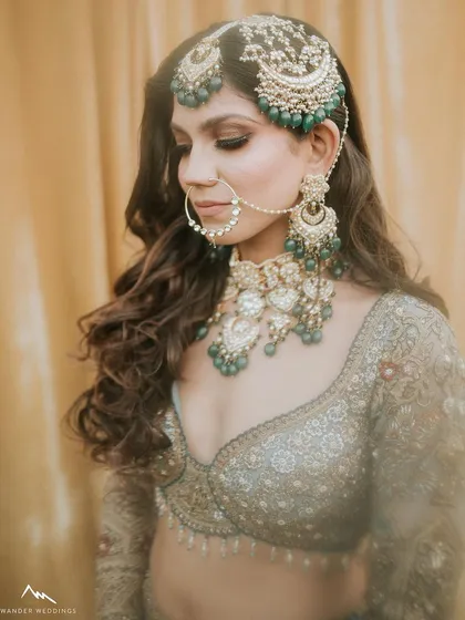 A detailed shot of the bride's profile, focusing on her intricate jewelry and the soft, smokey eye makeup that complements the green stones.