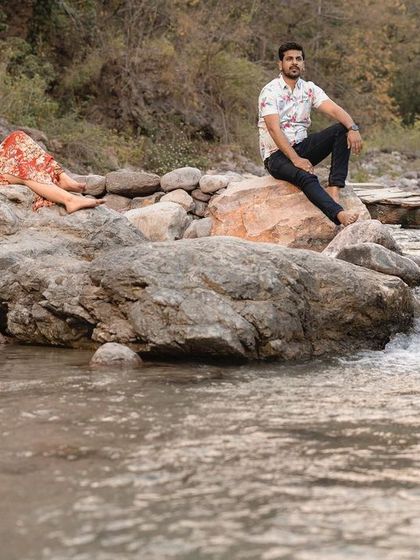 A wide-angle view of the couple relaxing by the river, showcasing the peaceful and beautiful environment of their pre-wedding shoot.