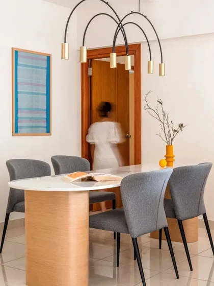 The dining area features a custom table with a marble top and curved plywood base. The sculptural brass and black pendant light acts as a centerpiece, adding a touch of modern elegance.