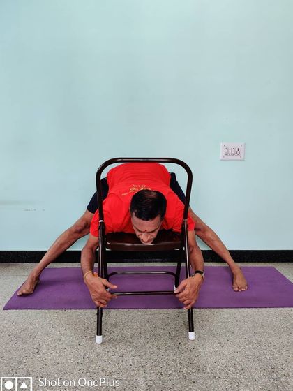 A variation of Prasarita Padottanasana (Wide-Legged Forward Bend) using a chair to deepen the stretch and release the spine.