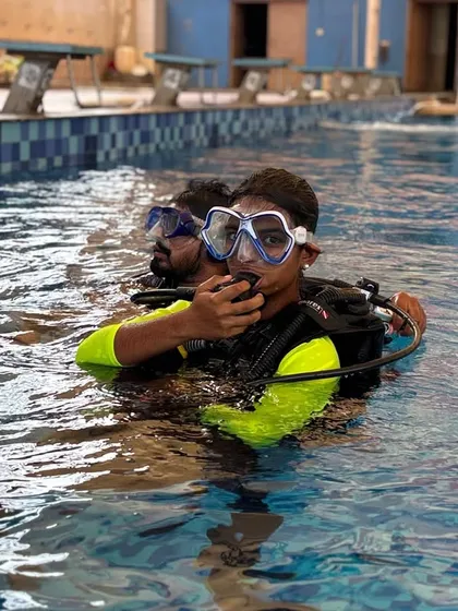A student practices using the breathing apparatus at the surface of the pool, with an instructor right by his side.