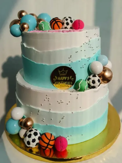 A stylish two-tier cake decorated with fondant sports balls like basketballs and soccer balls, perfect for a young athlete's party.
