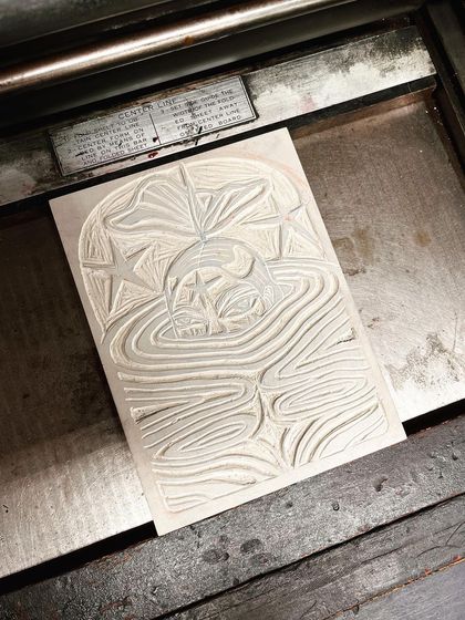 The carved linoleum block on the printing press, ready to be inked.