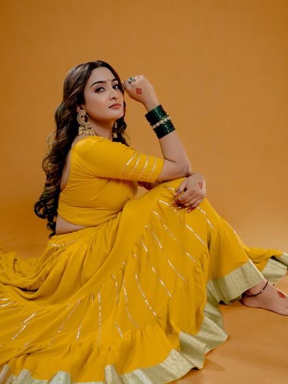 A graceful seated pose that highlights the full traditional outfit against a warm, solid background. This type of shot is ideal for lookbooks and editorial spreads.