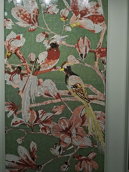 A close-up of a glass mosaic mural depicting birds and flowers. Each piece is carefully placed to create a vibrant, detailed artwork that adds a splash of color and elegance.
