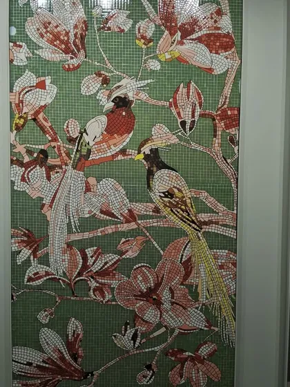 A close-up of a glass mosaic mural depicting birds and flowers. Each piece is carefully placed to create a vibrant, detailed artwork that adds a splash of color and elegance.