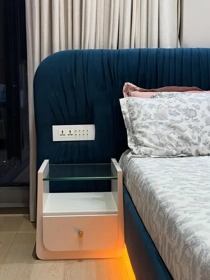 Detail of the bedside table and the pleated velvet headboard. The design includes conveniently placed electrical sockets for charging devices.