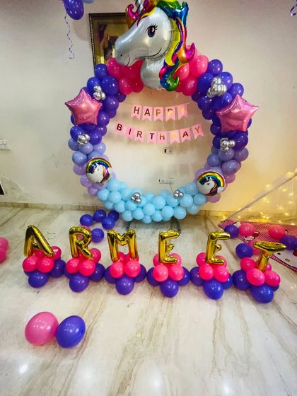 A unicorn-themed ring decoration with the name 'ARMEEN' spelled out in foil balloons. The purple and pink balloons create a magical look for this home party.