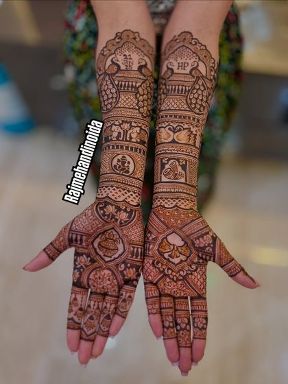 A very detailed and symmetrical bridal design. It includes peacocks, elephants, and the couple's initials "HP," all balanced perfectly across both arms.