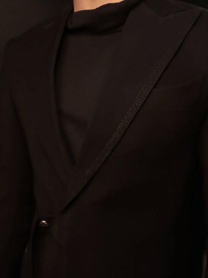 A detail shot of the asymmetric black jacket, highlighting the textured, sparkling trim on the lapel. It's these small touches that elevate a bespoke garment.