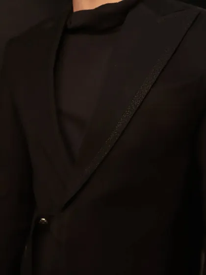 A detail shot of the asymmetric black jacket, highlighting the textured, sparkling trim on the lapel. It's these small touches that elevate a bespoke garment.
