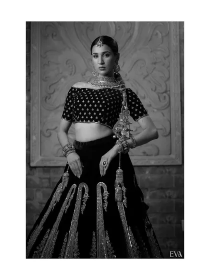 A timeless black and white portrait of the model in a traditional lehenga. This artistic choice emphasizes the texture, embroidery, and powerful silhouette of the bridal attire.