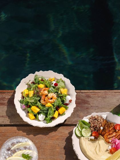 Lunch by the pool, featuring a fresh mango and shrimp salad alongside a plate of grilled chicken with quinoa and hummus.