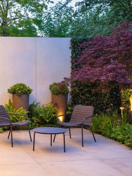 A modern patio designed for quiet contemplation. This space features a minimalist furniture set, large planters, and subtle uplighting against a feature wall, creating a chic and tranquil corner.
