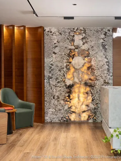 The luxurious lobby of Meghana Foods' corporate office features a backlit onyx wall as a stunning focal point. This space balances opulent materials with warm wood shelving and plush seating, creating an extravagant and welcoming entrance that immediately communicates the brand's prestige.