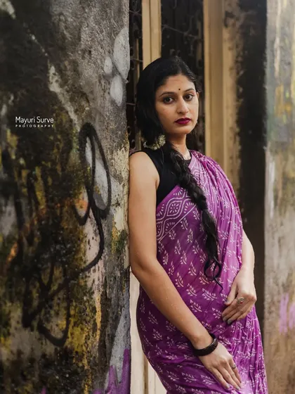 A strong, direct portrait against a textured, weathered wall. The model's gaze is confident, and the contrast between her vibrant purple saree and the gritty backdrop makes for a compelling image.