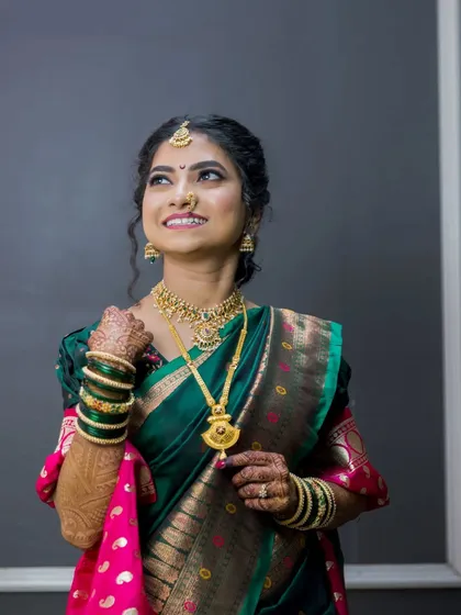 An elegant portrait of a bride in a beautiful green and pink saree, looking up with a hopeful and happy expression.