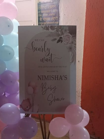 A welcome sign for a 'We Can Bearly Wait' themed baby shower. The sign is placed on an easel and surrounded by pastel-colored balloons.