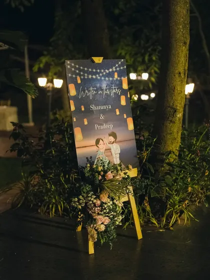 The custom welcome sign lit up at night, surrounded by lush greenery and soft lighting.