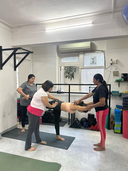 A three-person assist for a backbend, demonstrating the layers of support available in our community-focused classes.