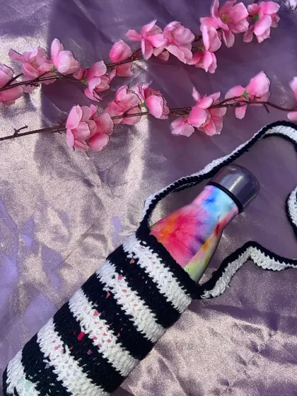 A handmade crochet bottle cover with black and white stripes. It has a long strap so you can carry your water bottle hands-free.