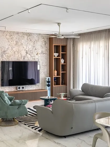 The living room from the 'Urban Oasis' project, showing a mix of textures and colors. A textured TV wall is flanked by wooden shelves, while teal armchairs add a pop of color.