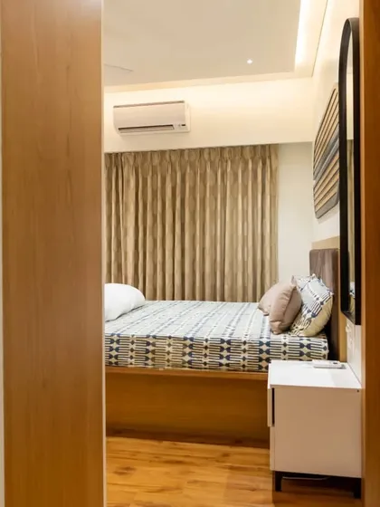 A view from the doorway into a beautifully appointed master bedroom. We designed the space with a veneer finish bed, matching wooden flooring, and soft curtains to create a warm and cohesive aesthetic.