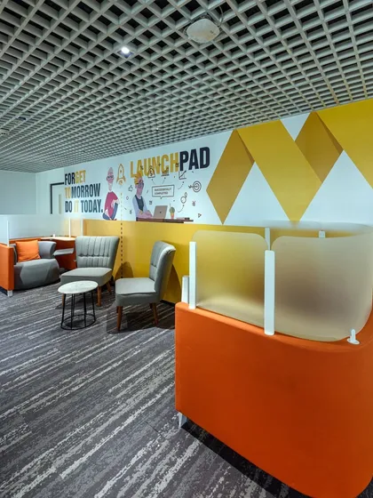 A breakout space with unique orange seating pods that offer a degree of privacy. The wall features a graphic with the motivational phrase "Forget tomorrow, do it today."