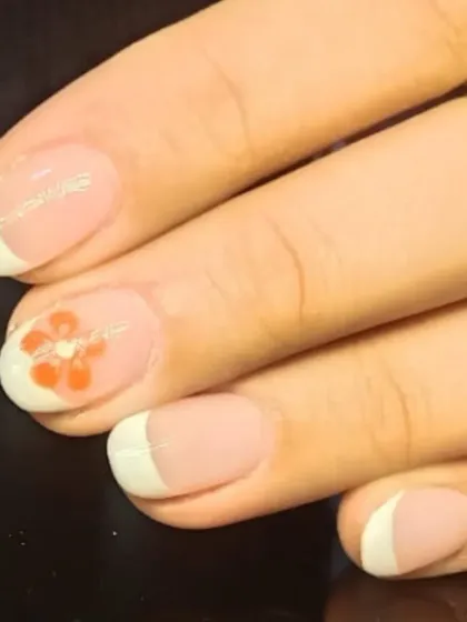 A simple and sweet French manicure with a single, delicate orange flower painted on an accent nail.