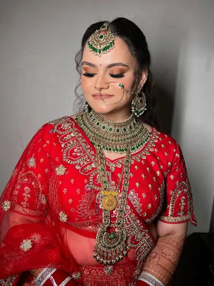 Eyes closed to showcase the warm, sculpted eye makeup that complements her red and green bridal attire.