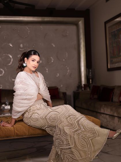 A moment of repose in the ivory sharara set, highlighting its intricate design and graceful silhouette.