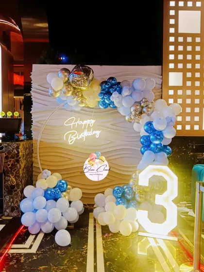 A modern half-arch balloon decoration in blue, white, and gold with a neon sign.